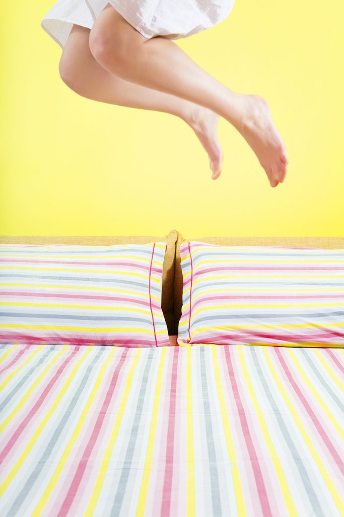 young woman jumping on bed with striped sheet