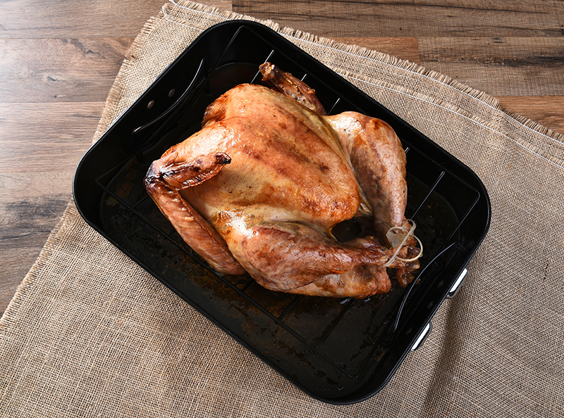 High angle view of a cooked turkey in a roasting pan. The golden brown Thanksgiving entree is in a black pan on a burlap table cloth.