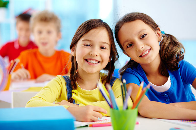 Portrait of two diligent girls looking at camera at workplace with schoolboys on background