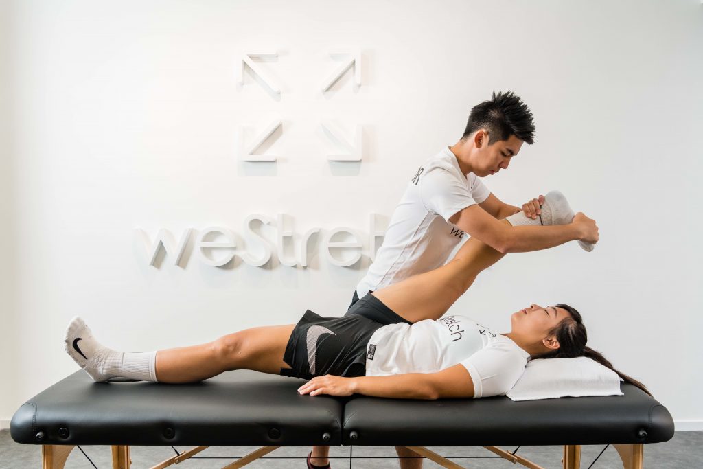 A man stretches a woman's leg during a rehabilitation session.