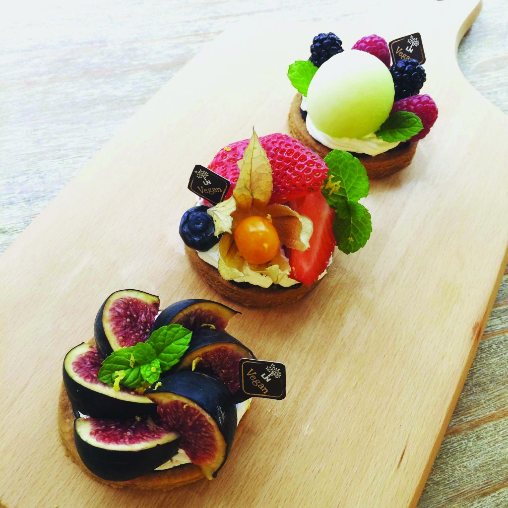 A row of vegan desserts on a wooden board topped with fruits.