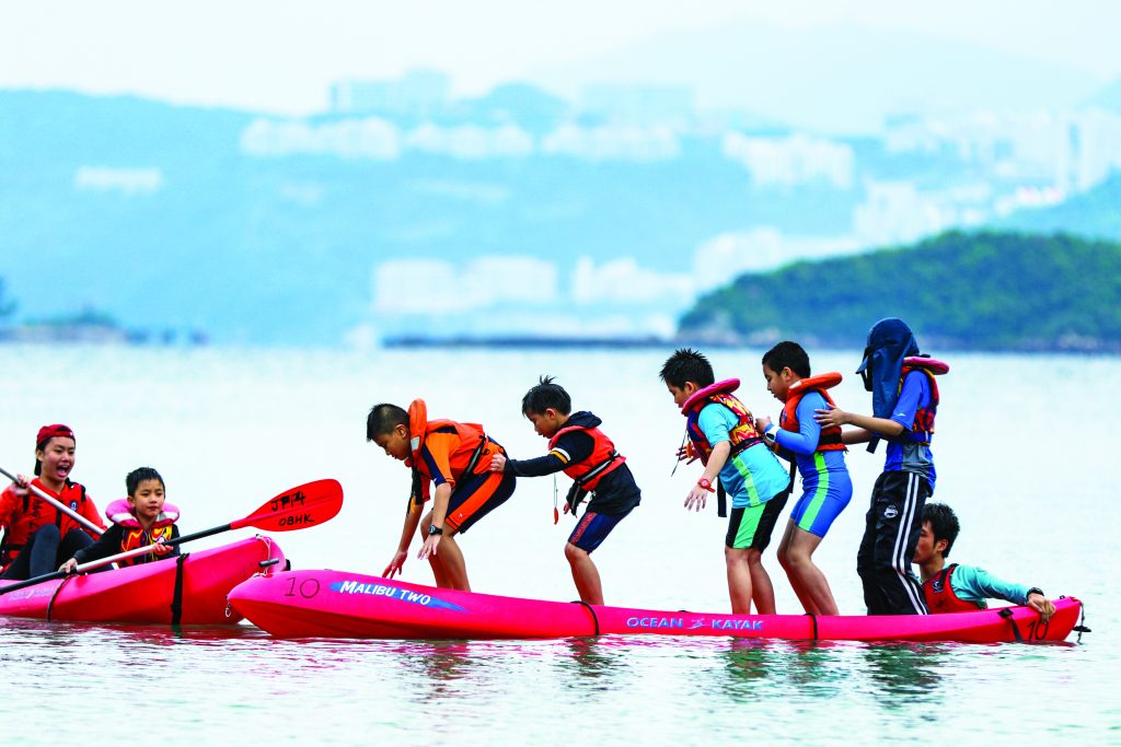 Several children stand on a kayak in the middle of the sea on an expedition organised by charity Outward Bound