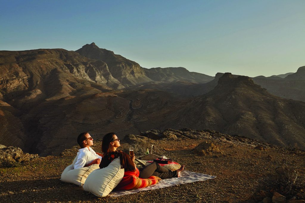 Two people sit on a blanket enjoying the view of Oman's countryside at Six Senses Zighy Bay resort.