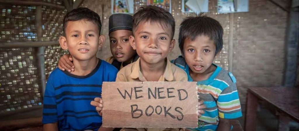 Four young children hold a sign asking for books, recipients of the Bloom Books charity from Lamma Book Club