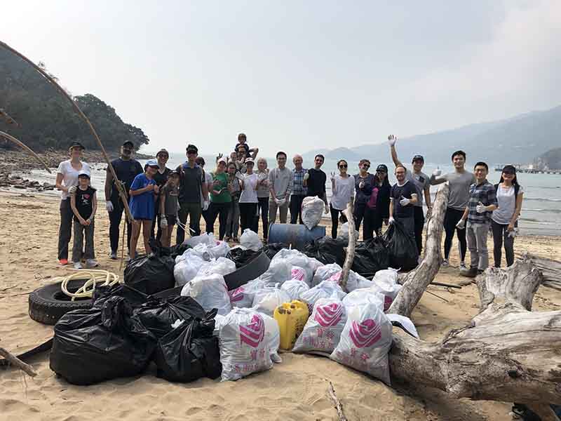 A group of people stand around a pile of collected rubbish on a beach in Hong Kong