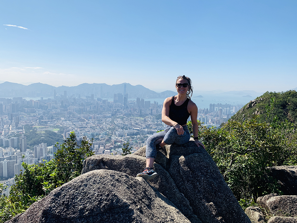 A woman sits on rock during a hike, part of her self care routine. 