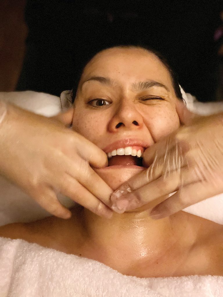 Sarah Fung lays on a treatment table with gloved hands in her mouth, during a Buccal face massage in Hong Kong