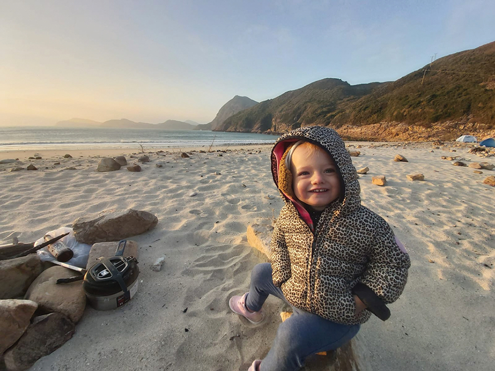 A young girl sitting on a beach at Pak Lap Wan, a family-friendly campsites in Hong Kong.