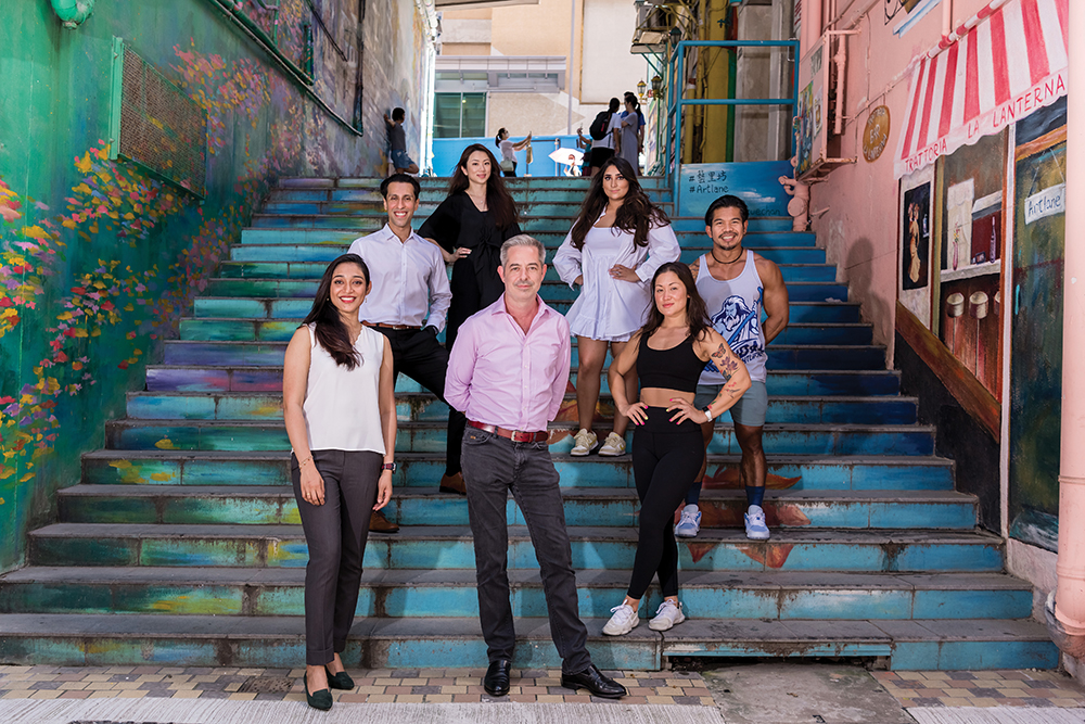 A group of seven people who are pandemic entrepreneurs stand on colourful steps in a Hong Kong neighbourhood.